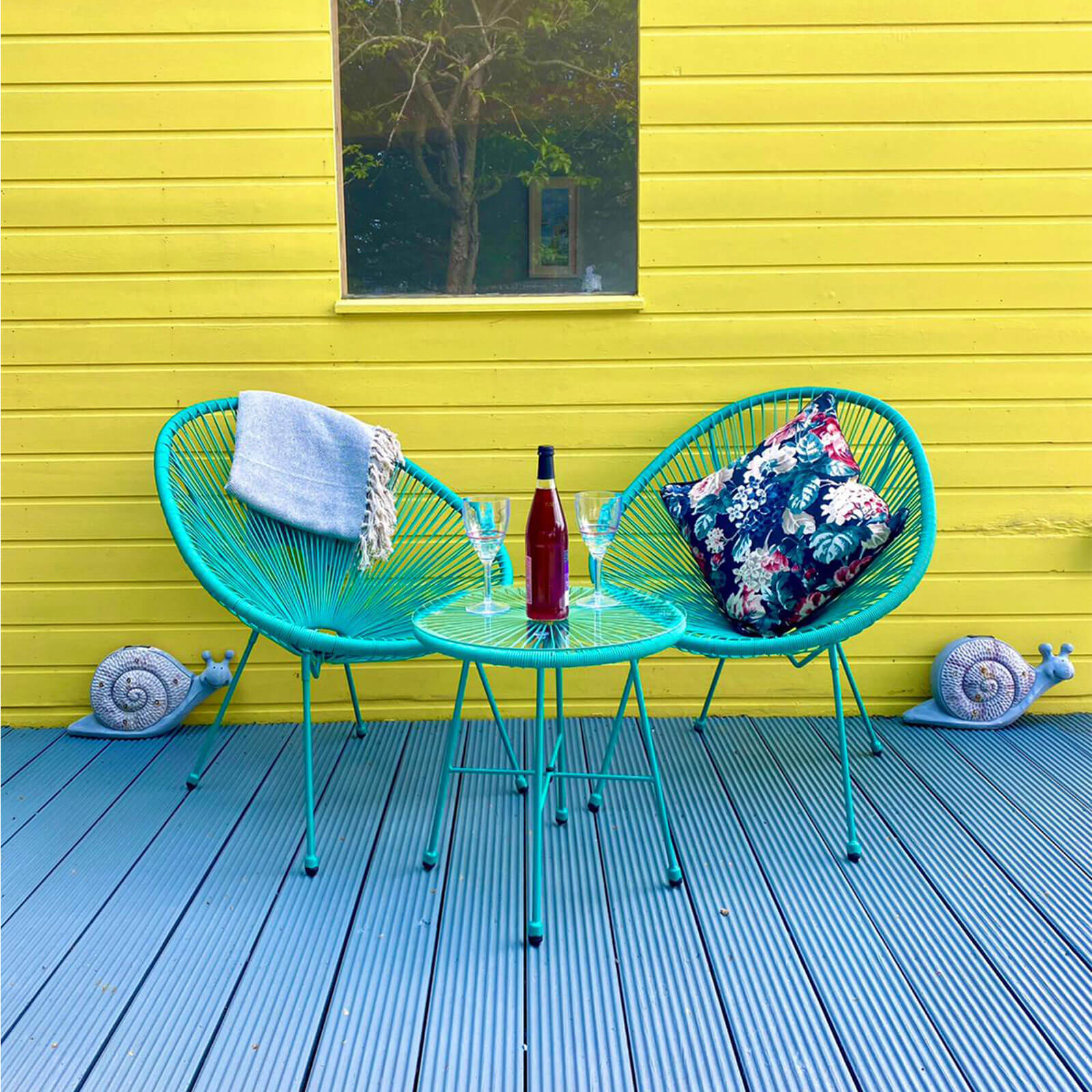 emerald green bright rattan egg chair bistro set with 2 rattan egg chairs and one bistro coffee table with glass table top sitting on a decking in a garden with summer house