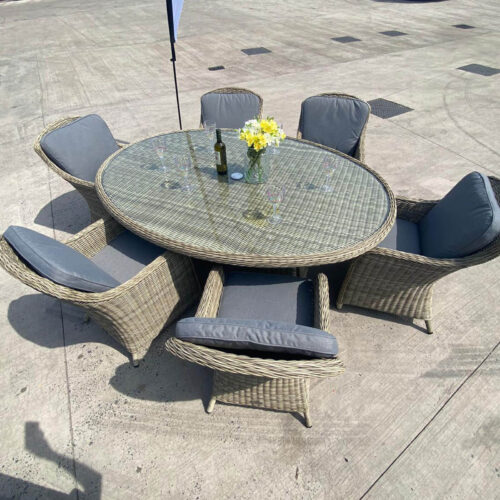 ballintoy 6 seat rattan garden dining set with low back imperial chairs in beige rattan and grey cushions in a yard dressed with flowers on a sunny day
