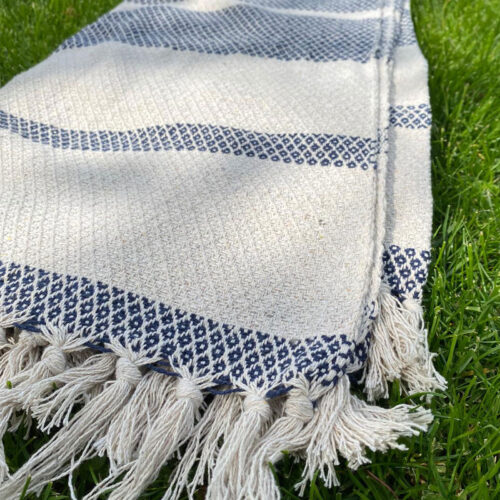 marina blue and cream throw with woven diamond design and tassel ends on the grass for home living accessories or garden furniture decoration