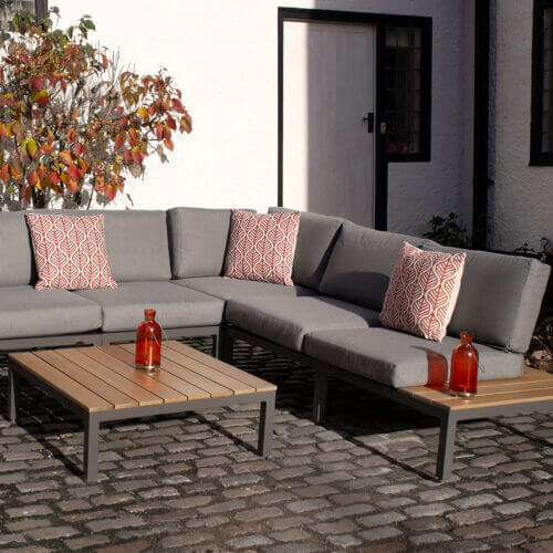 Ballyholme 6 seat modular corner sofa and coffee set with grey cushions and brown wooden table made from aluminium in a garden setting